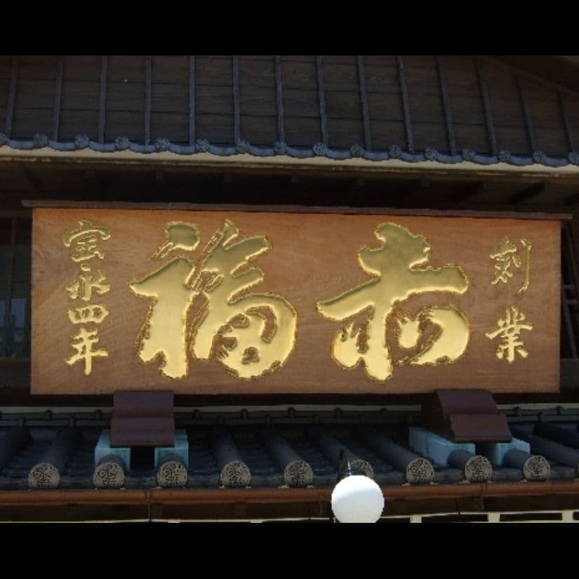 木の看板で文字が金色、屋根の上に大きな看板　銅板で台が出来ている
