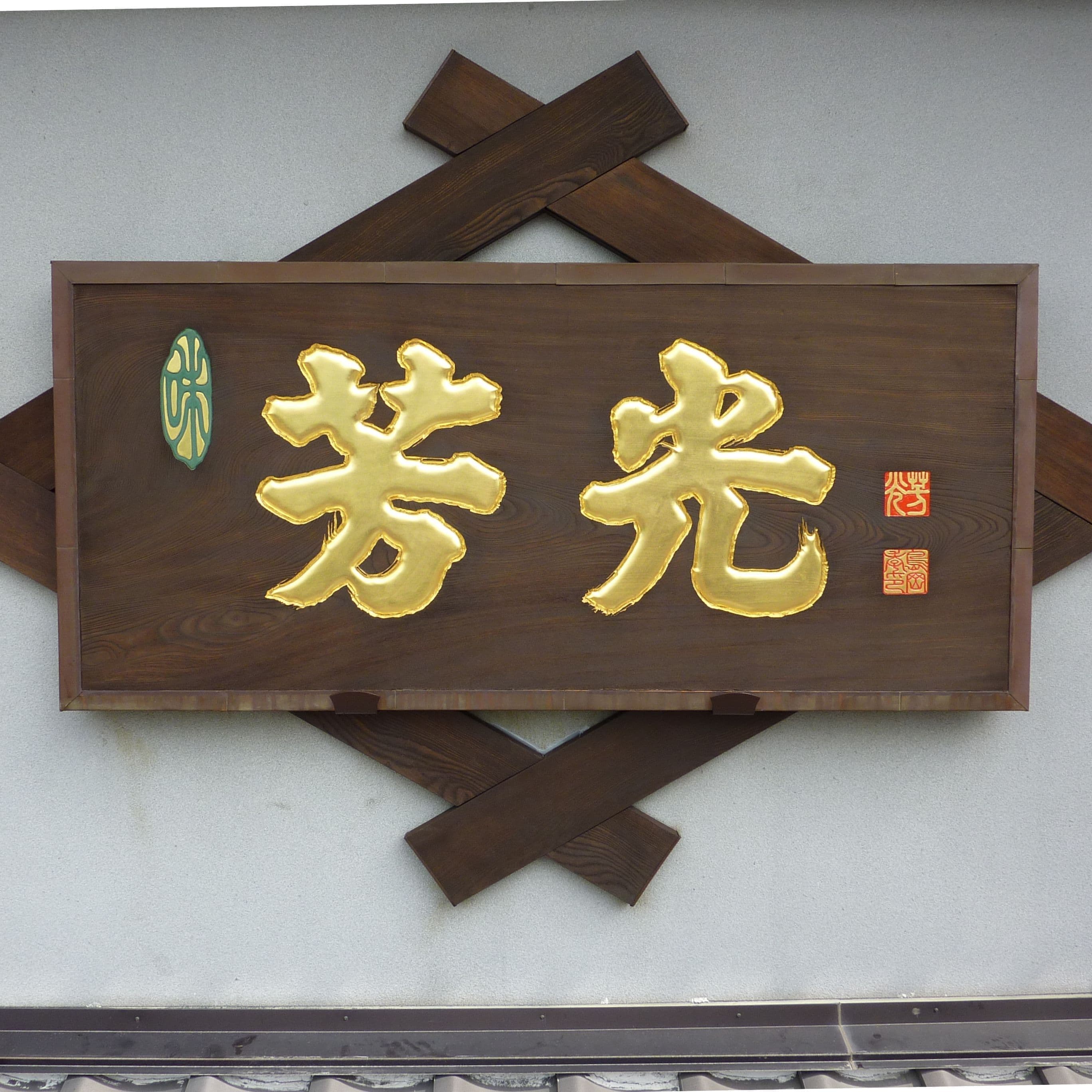 壁に木の看板が設置され、文字は金色、落款も彫刻されている