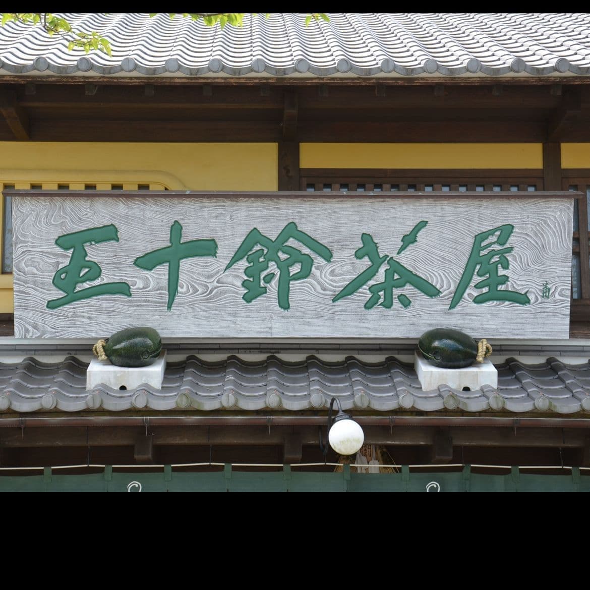 入り口の上に木目を加工して白くしてある木の看板で文字は緑青、和風を感じさせる