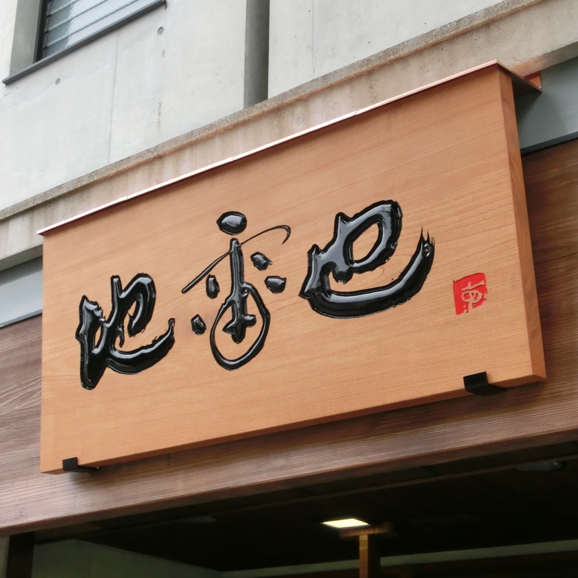 天むす店の屋外の壁に木の看板、文字が彫ってあり黒光りしている