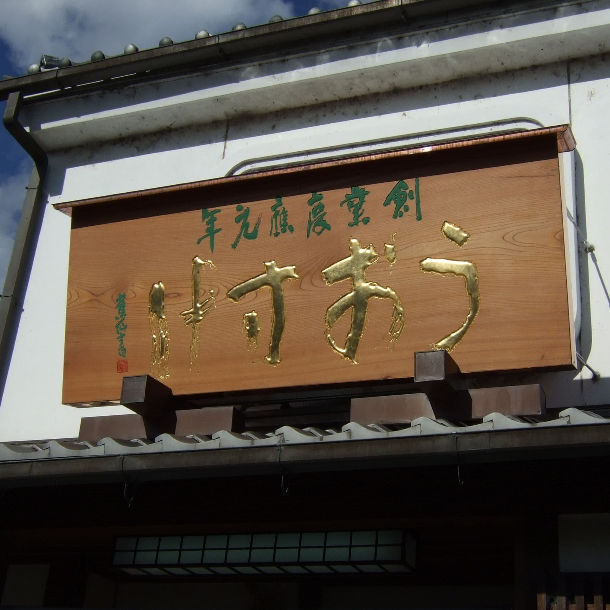 瓦の上に木の板で金色文字が彫ってあり和風の印象の看板