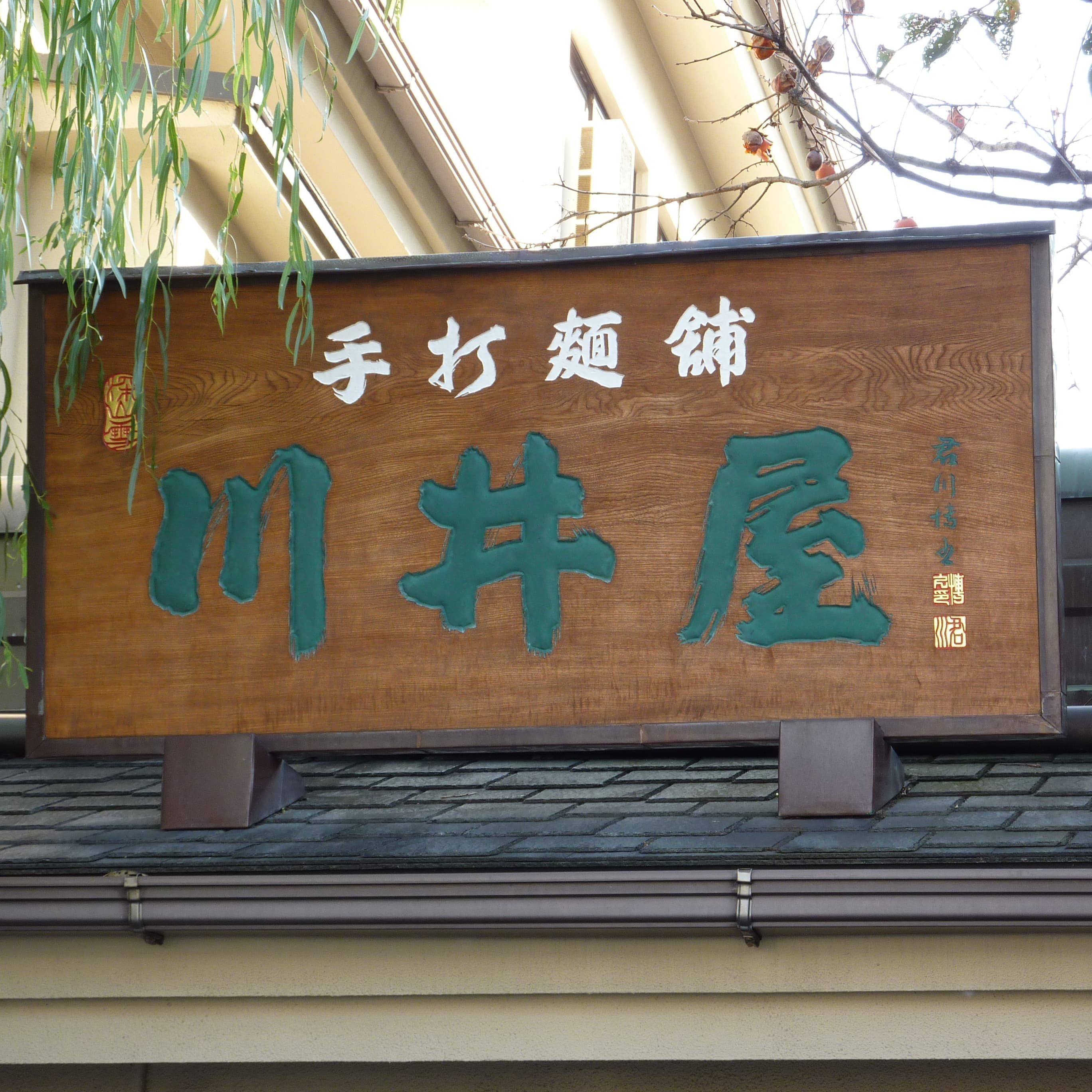 有名手打ちうどん店の店頭で木の板に屋号が彫ってある看板