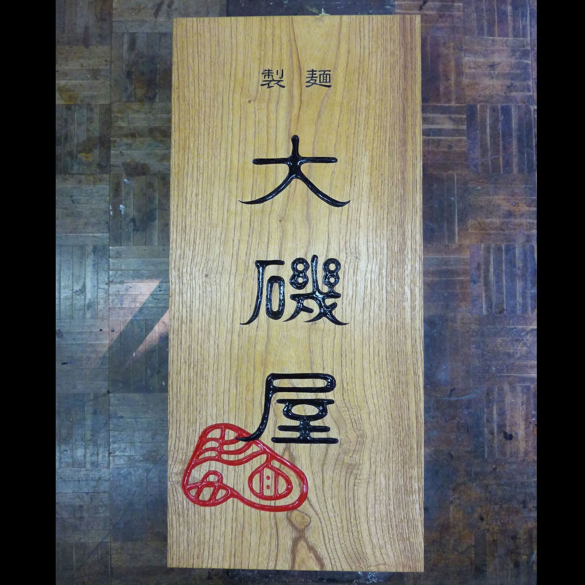 木目のきれいな板にロゴマーク入りの製麺所の彫刻看板