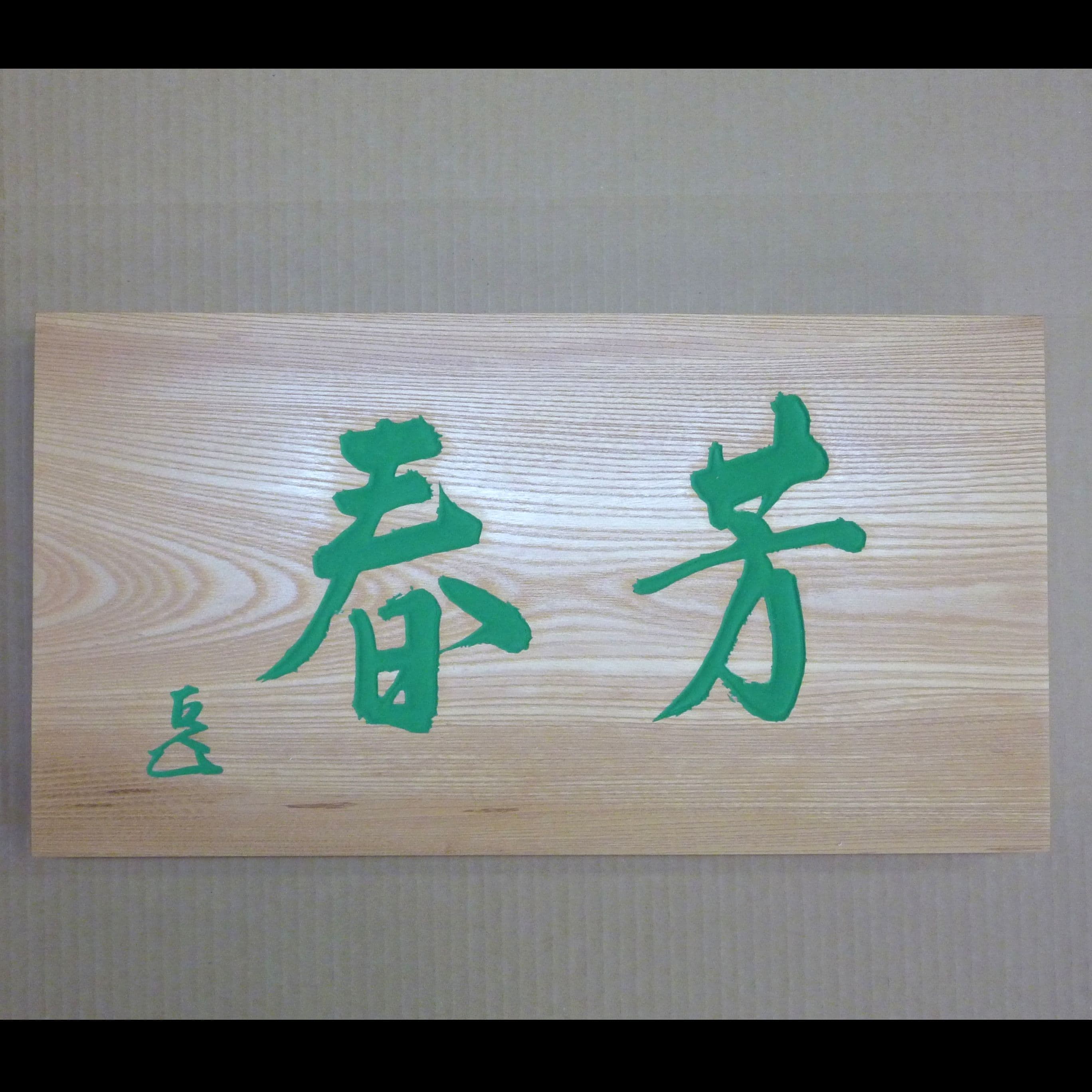 ケヤキの木の板に緑の文字で揮毫と花押が書いてある彫刻看板、扁額