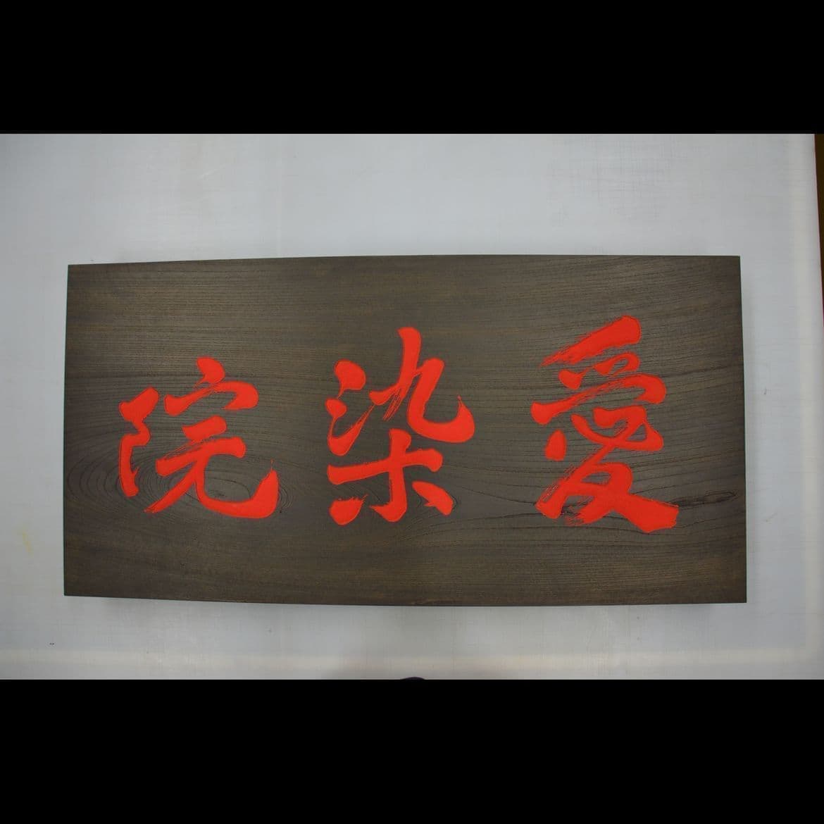 濃い色の木の板に鮮やかな朱色の文字でお寺の名前が彫ってある看板、扁額