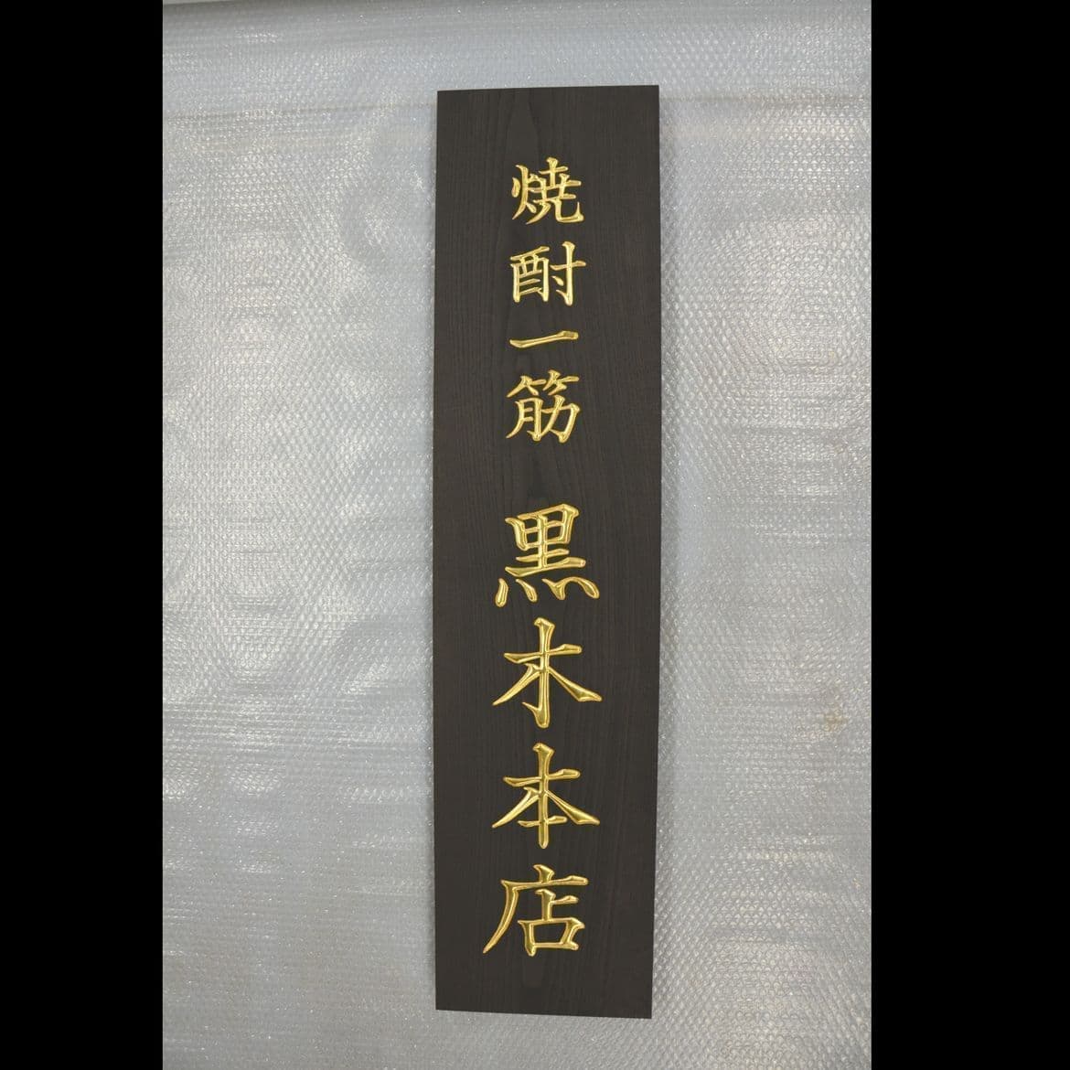黒い木の板に金文字で社名が彫刻されている表札、看板
